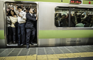 A packed Yamanote line train in Tokyo with men and women struggling to board.